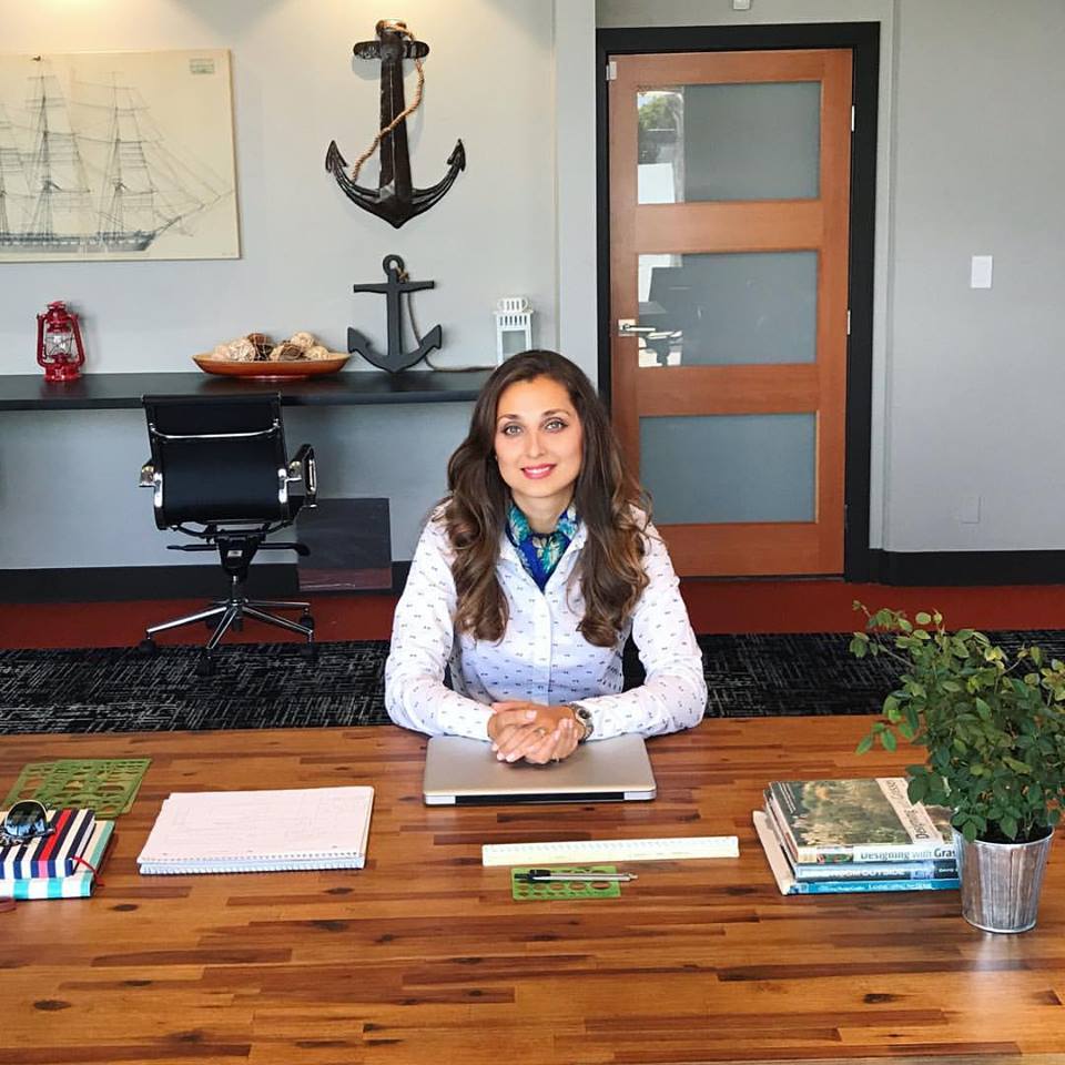 Kristina sitting at a wooden table in a design studio, working.