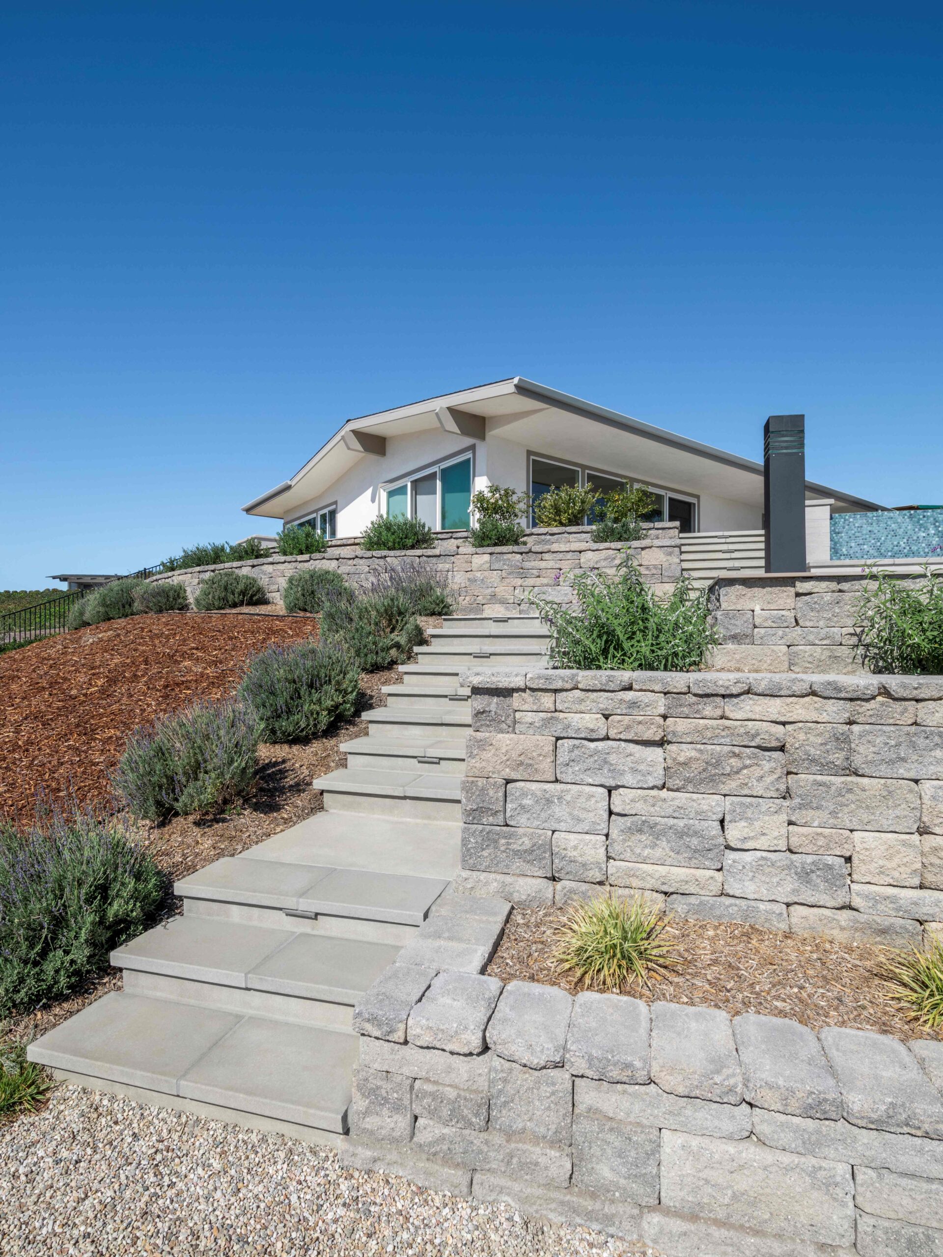 segmental retaining wall in gray color, with concrete steps, hillside with plants.