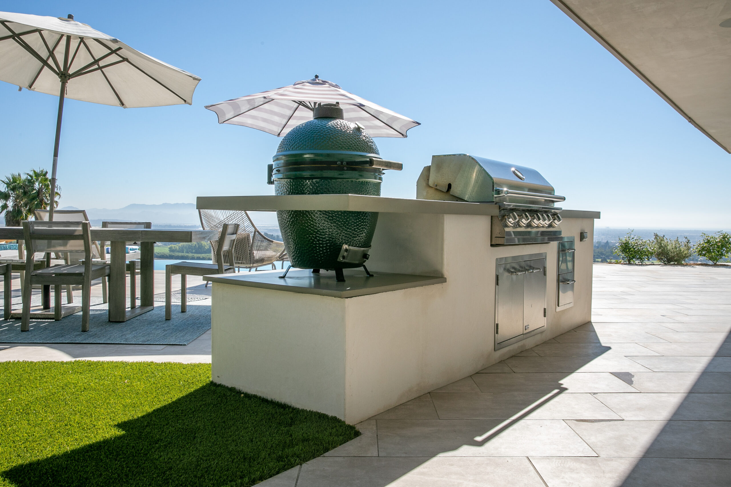 Luxury outdoor kitchen with built-in grill, Big Green Egg smoker, dining space, and panoramic views in Ventura, California.