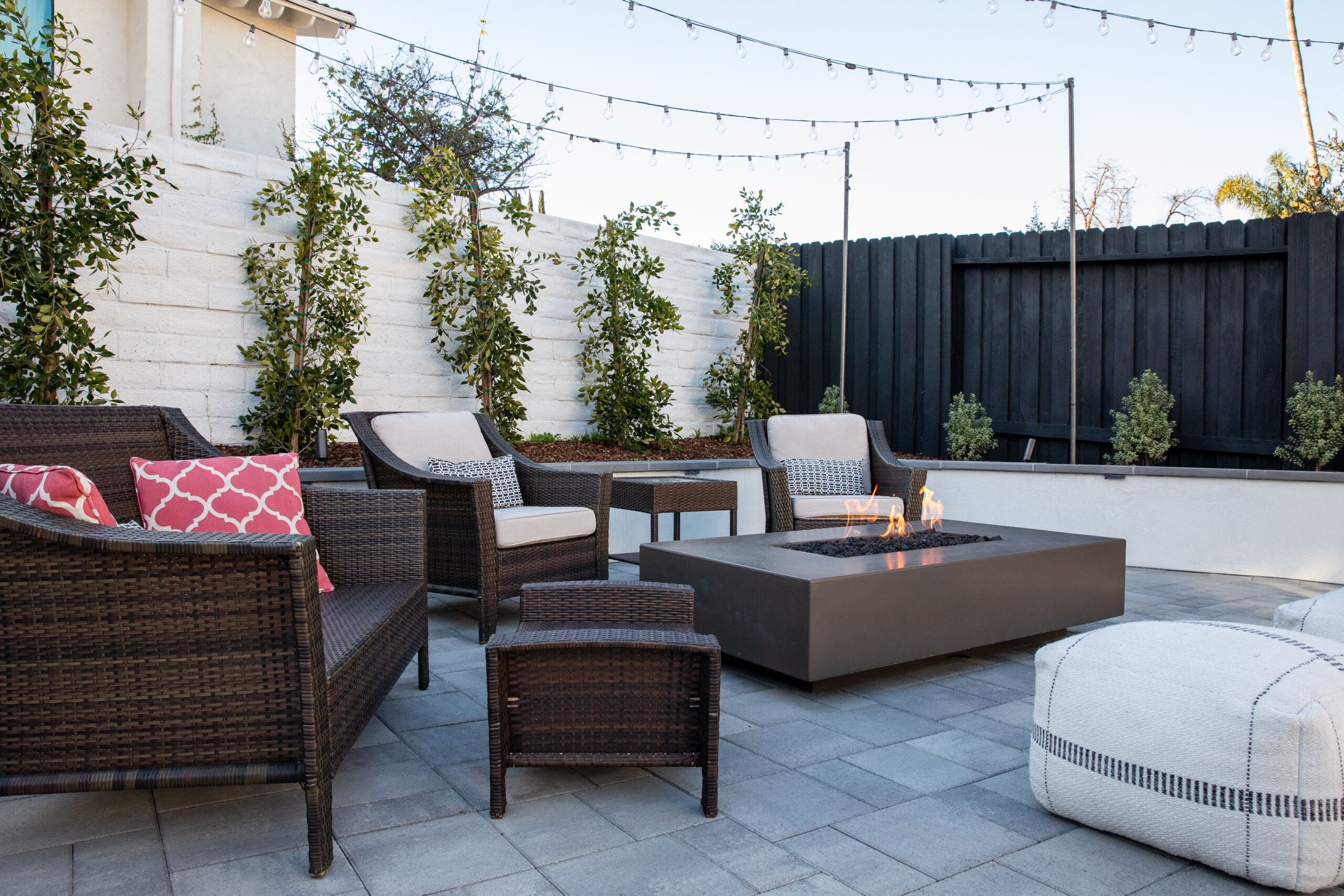 Modern outdoor fire pit patio with lounge seating, string lights, and concrete pavers designed for outdoor entertaining.