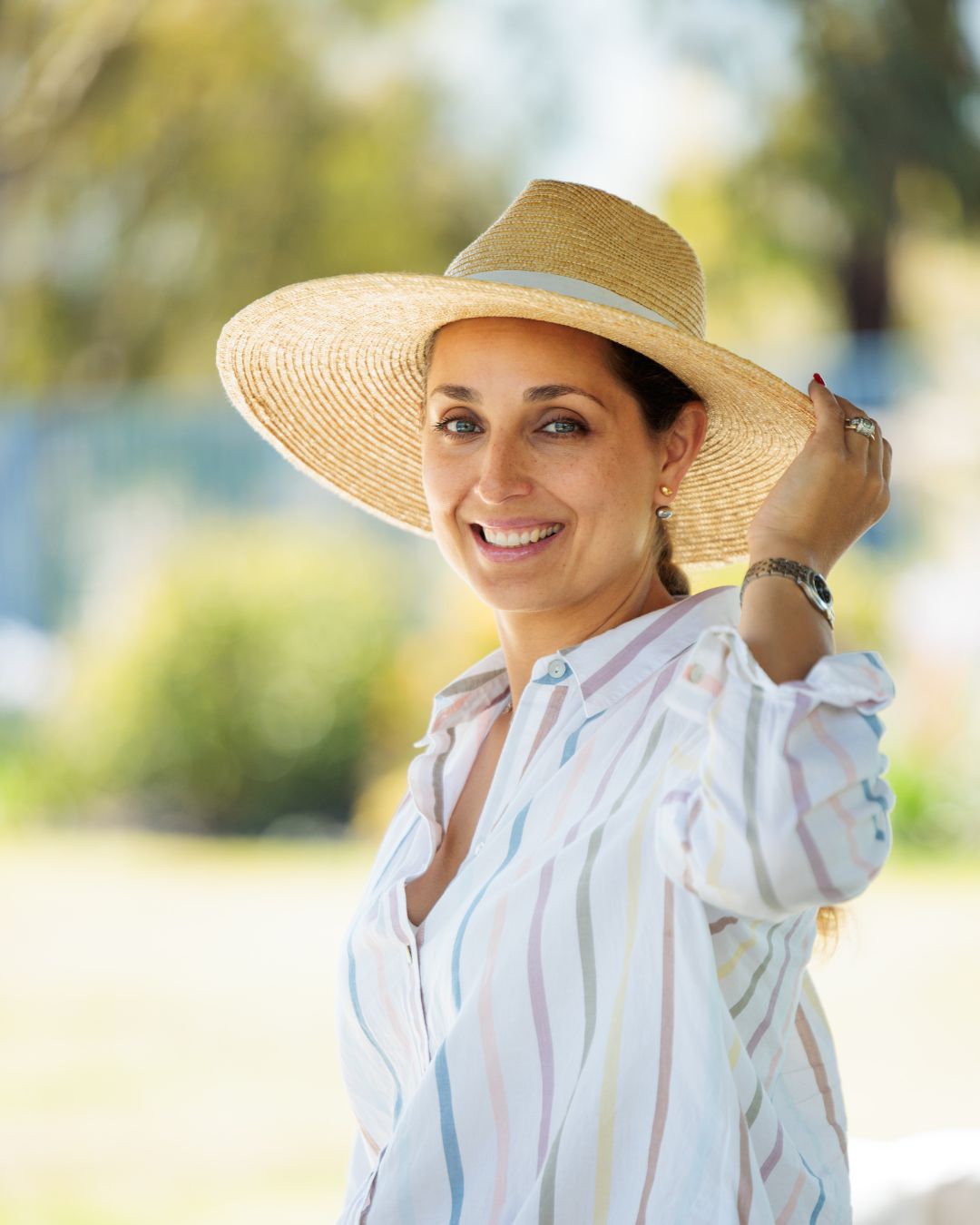 Woman smiling and holding a straw hat with outdoor landscape in the background